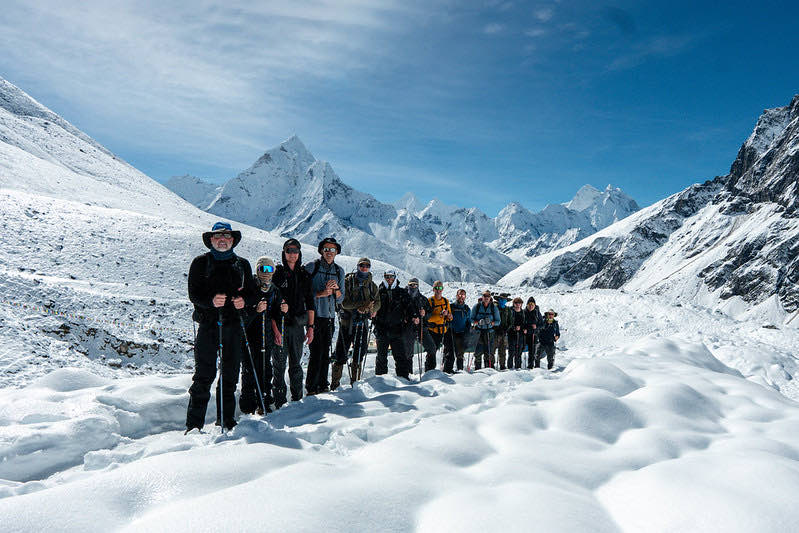 A trekking group lined up on a snowfield below Himalayan peaks